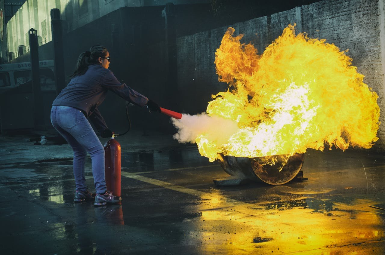 Services A woman uses a fire extinguisher to put out a large flame in an outdoor setting, showcasing fire safety.